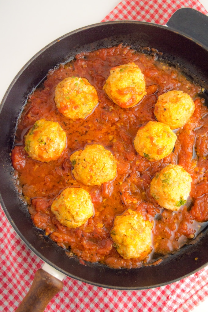 A cast iron skilled on a table filled with nine turkey meatballs cooked in tomato sauce