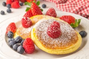 closeup of a plate with a fluffy pancake topped with raspberries